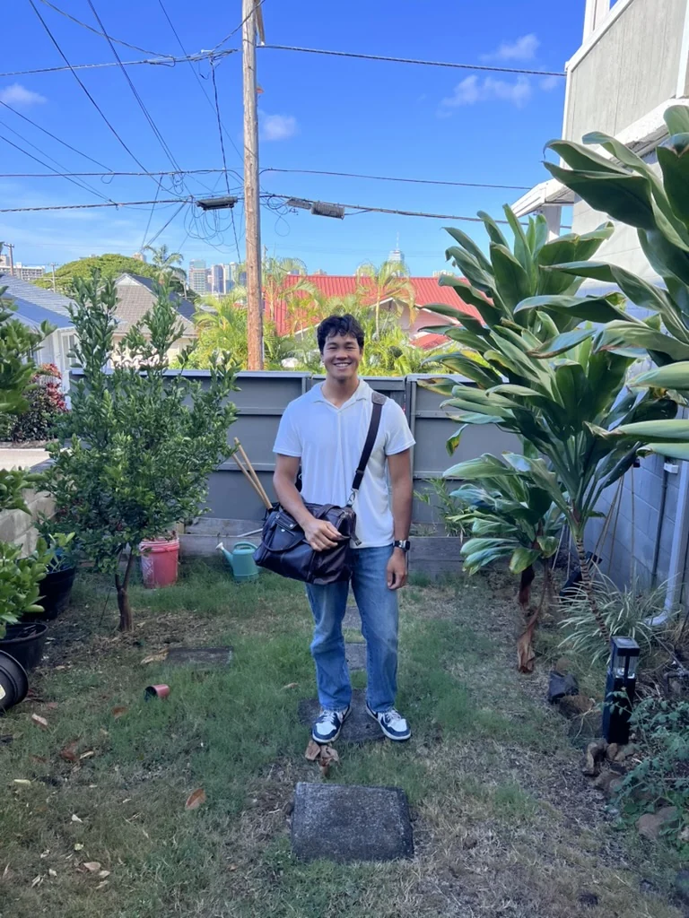 Bobo smiling in a backyard garden with a bag over his shoulder.