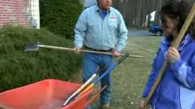Video still: two gardeners loading mulch into a red wheelbarrow beside a house.